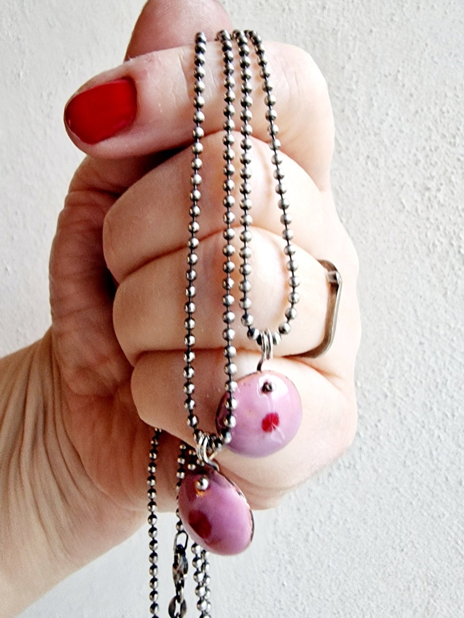 Debbie brösthalsband med hand som håller i kedjorna. Dekorativa med rosa och röd färg - Vatlings smycken